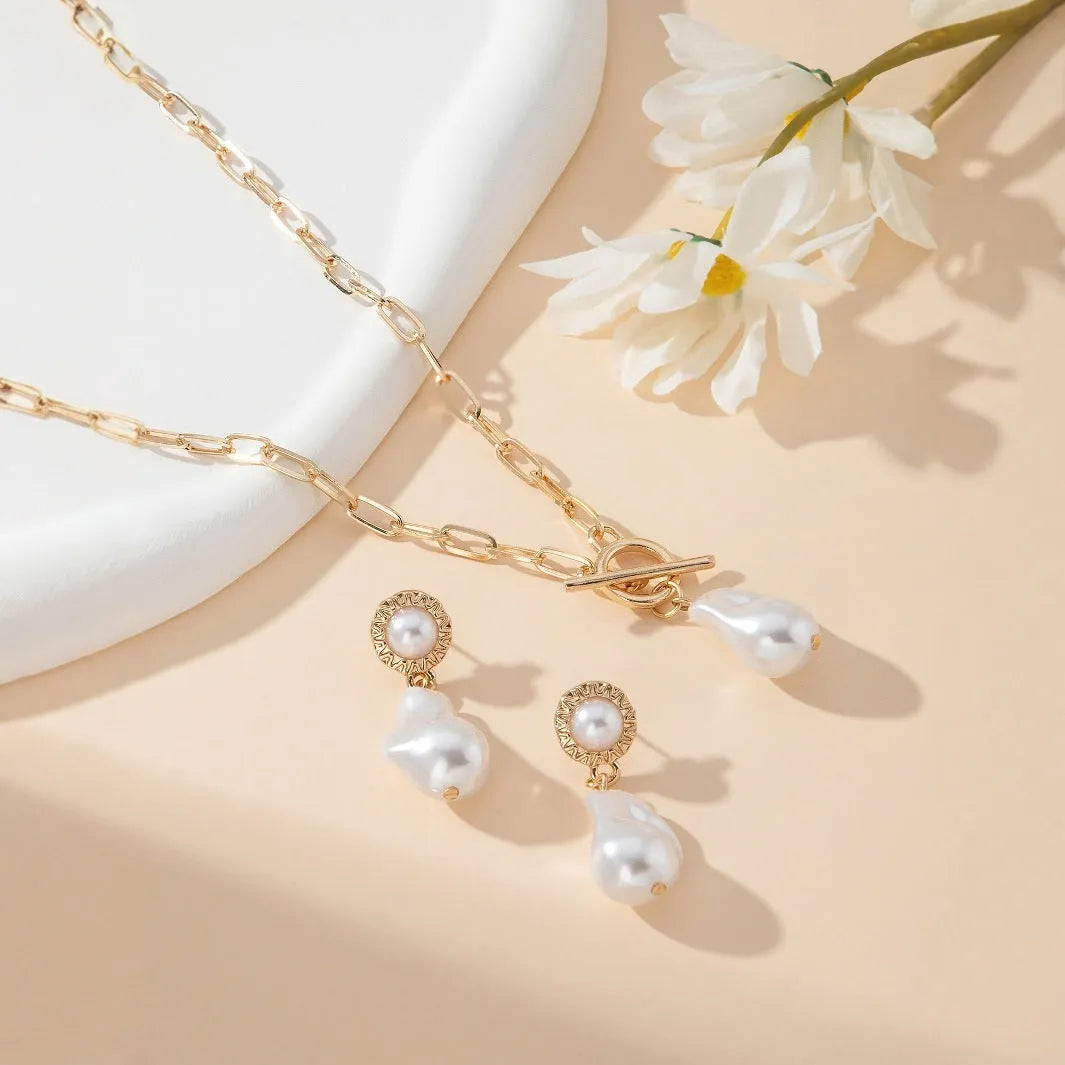 Gold-toned baroque pearl pendant necklace and matching stud earrings set on a dark background.