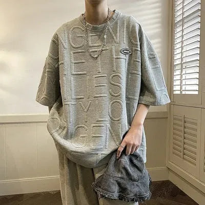 Man modelling a grey loose-fit T-shirt with a large retro-style graphic letter print on the front.