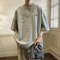 Man modelling a grey loose-fit T-shirt with a large retro-style graphic letter print on the front.