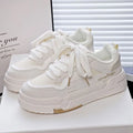 Beige children's platform trainers with cross shoulder straps and white rubber soles on a wooden floor.