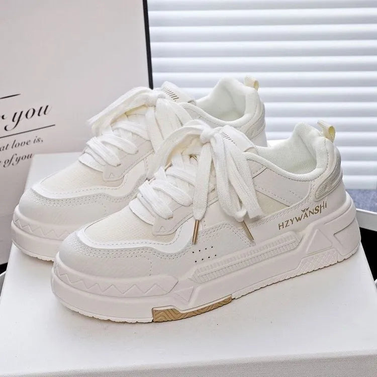 Beige children's platform trainers with cross shoulder straps and white rubber soles on a wooden floor.