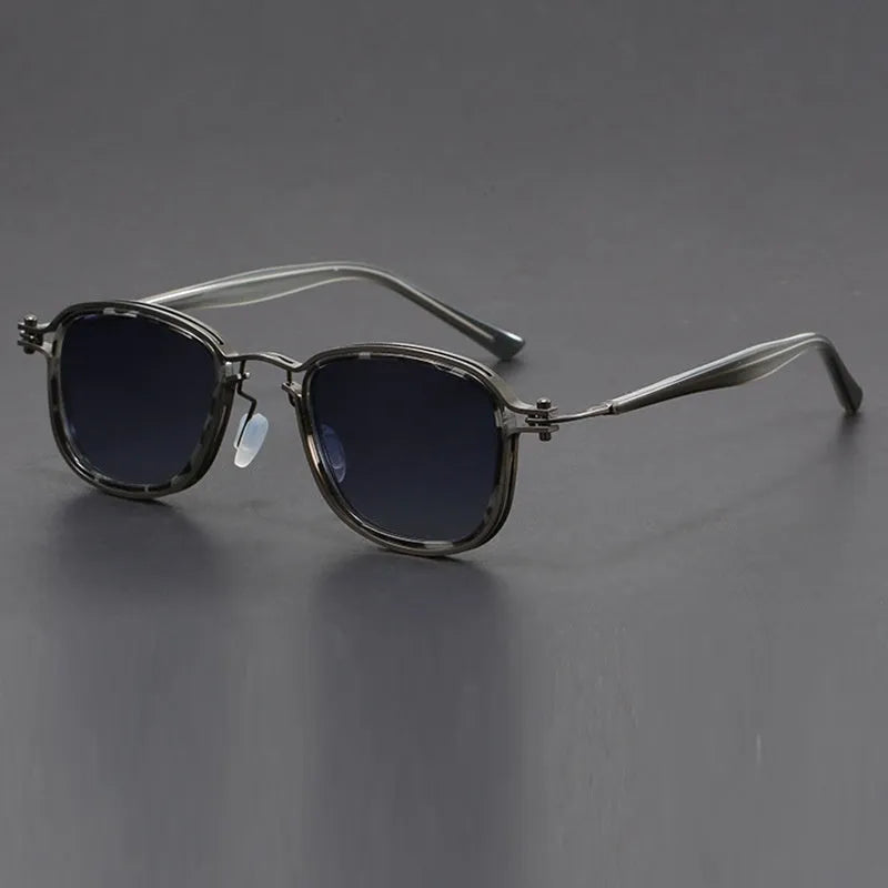 Retro square sunglasses with black gold frames and grey AC lenses on a wooden surface.