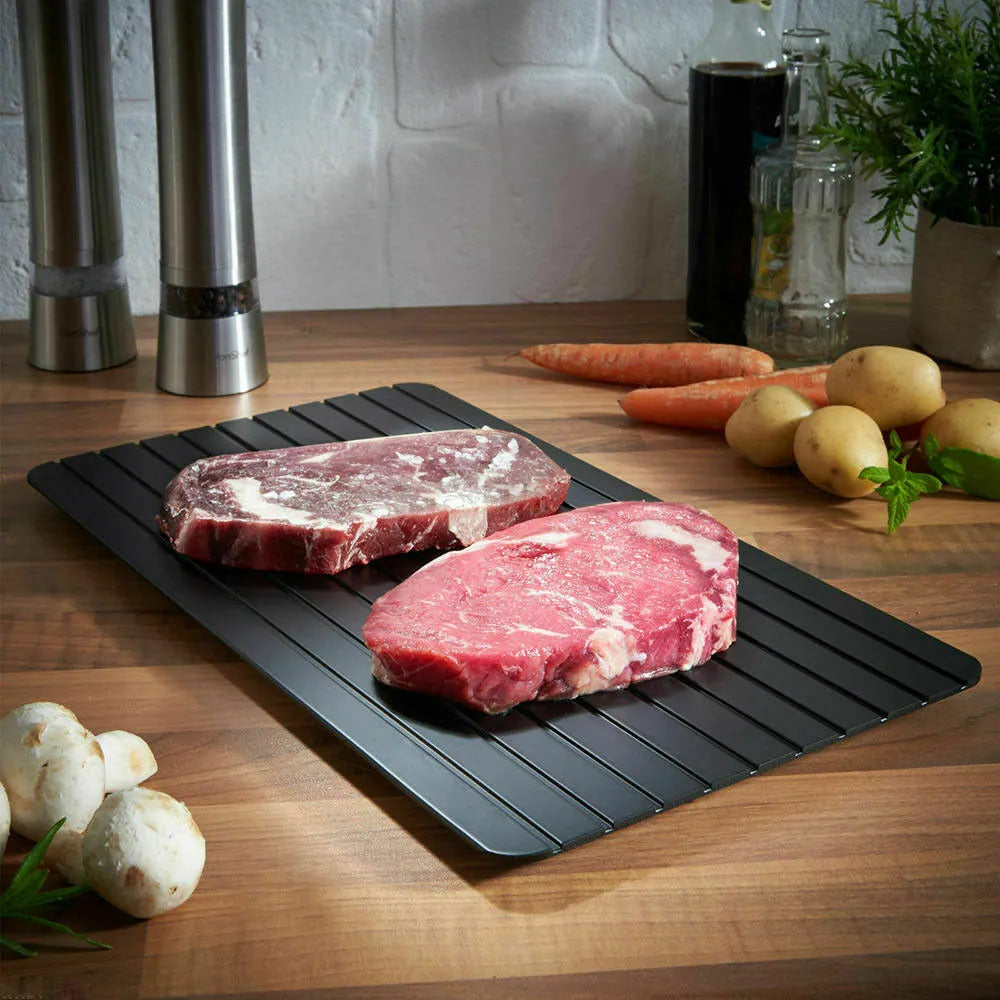 Black aluminium fast defrost tray for thawing frozen food on a kitchen counter.
