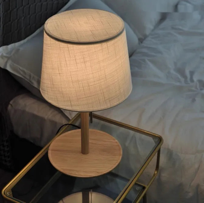 Walnut coloured solid wood bedside lamp with a white fabric lampshade and a cable switch