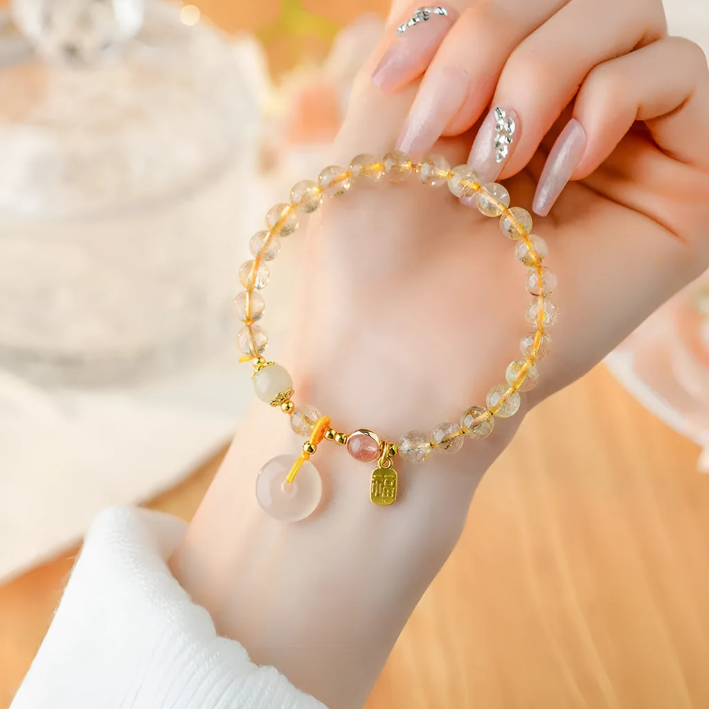 Gold rutilated quartz bracelet with a peace buckle pendant and geometric safety clasp.