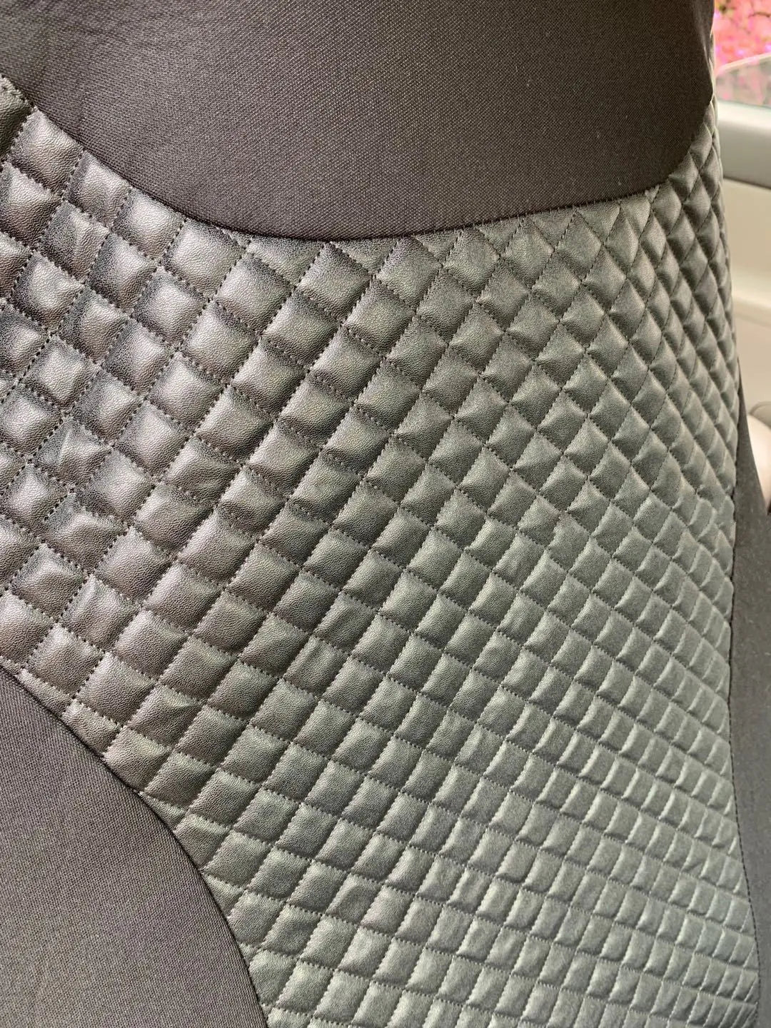 Black quilted automotive seat cover made of PU and polyester fabric with plastic attachment hooks.