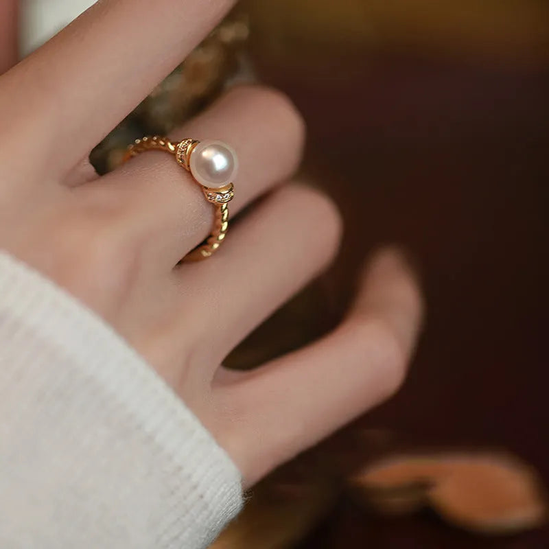 Antique finish copper ring with geometric twist and central inlaid pearl on a wooden background
