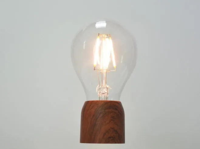 Magnetic levitation desk lamp with a floating glass bulb above an imitation wood base.