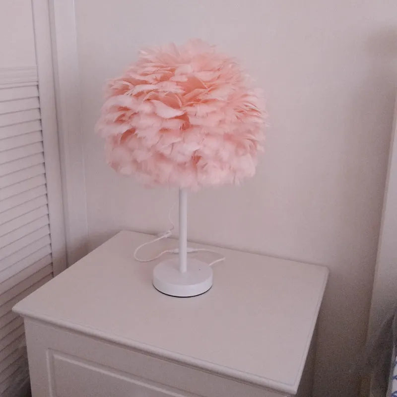 Handmade feather table lamp with metal base, white feathers, and remote control on a wooden bedside table