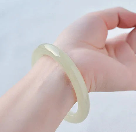 A polished natural jade round bar bracelet showing a winding silk texture on its surface.