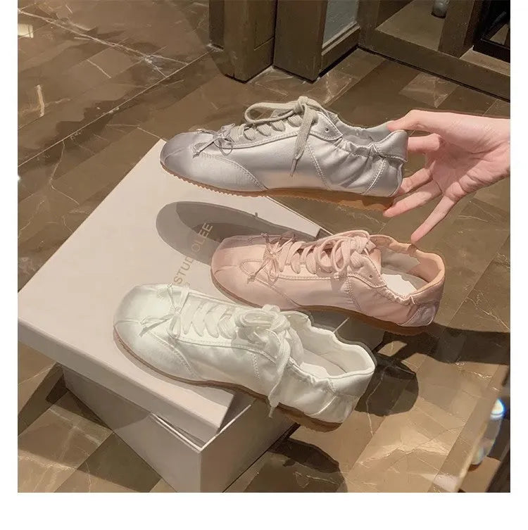 Women's champagne pink satin ballet flat shoes with a round toe and white front lace-up detail.