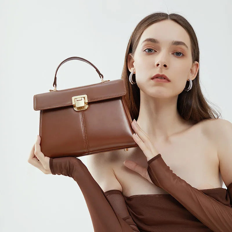 Women's black genuine leather shoulder bag with a clasp, shown with adjustable strap and open to reveal internal zippered pocket.