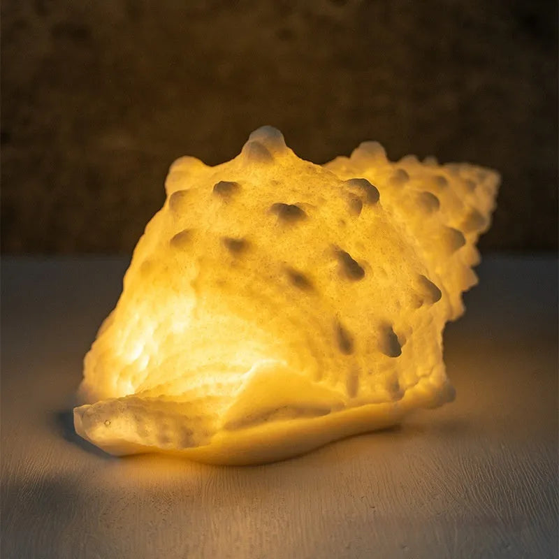 Small geometric night lamp with built-in battery in conch colour, dimensions 13 by 19 by 11 cm, on a bedside table