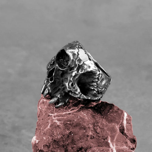 Close-up of a silver-toned alloy ring with a raised one-eyed skull design on a black background.