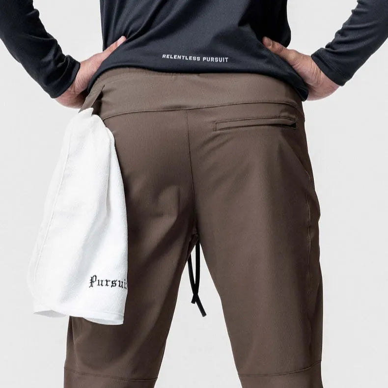 Man wearing dark grey loose-fit fitness trousers with tied ankle cuffs, made from quick-dry polyester fabric.