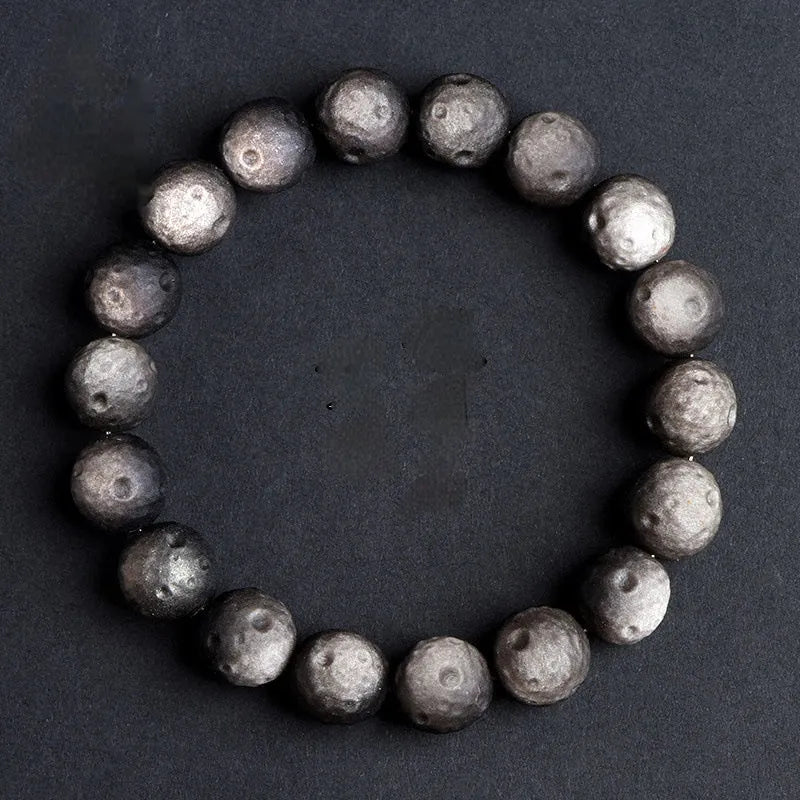 Natural obsidian crater ball bracelet in gold or silver stone colour on a wrist, showing textured bead surface.