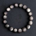Natural obsidian crater ball bracelet in gold or silver stone colour on a wrist, showing textured bead surface.