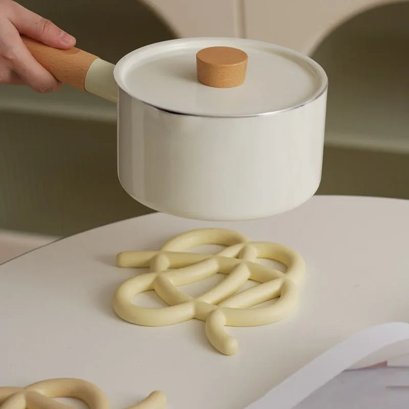 Irregular-shaped ceramic heatproof mat in a solid colour on a wooden table, protecting it from a hot pan.