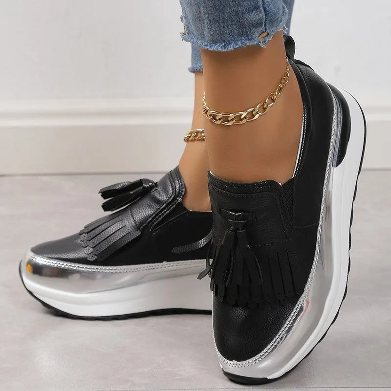 Women's black casual platform shoes with tassel decoration and a distinctive English muffin wedge heel.