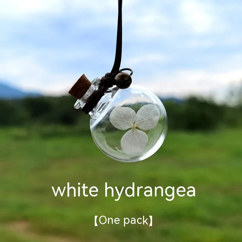 Glass car perfume pendant with preserved flowers inside, shown in a selection of different floral colours.