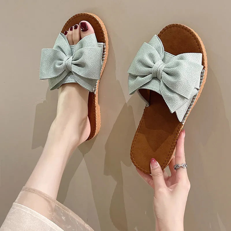 Women's beige suede slip-on sandals with a bow detail and soft rubber sole.