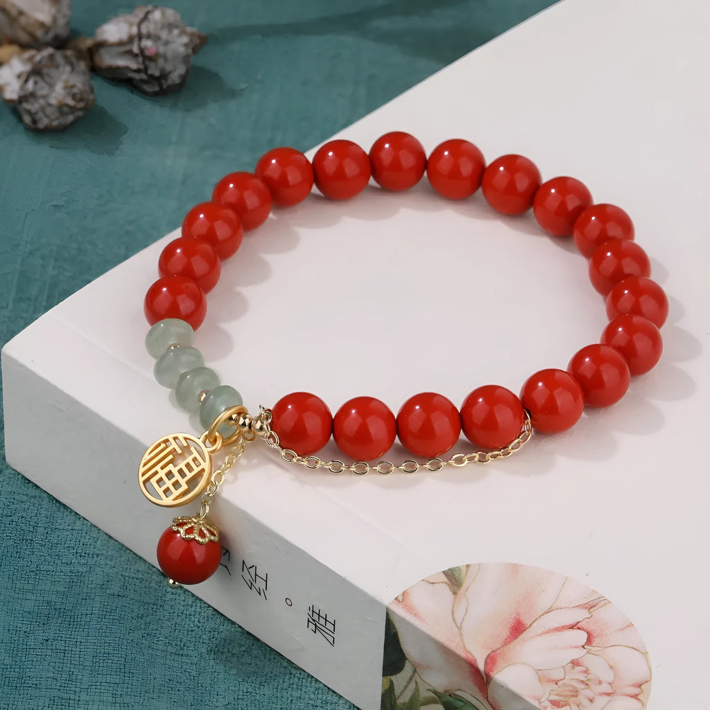 Women's red cinnabar bracelet with fu character charm, jade spacer bead, and tassel design