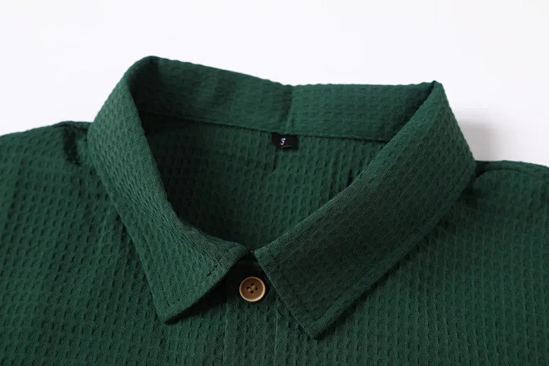 Dark green waffle patterned lapel polo shirt with short sleeves, two round metallic-texture buttons, and slightly arc-shaped hem.