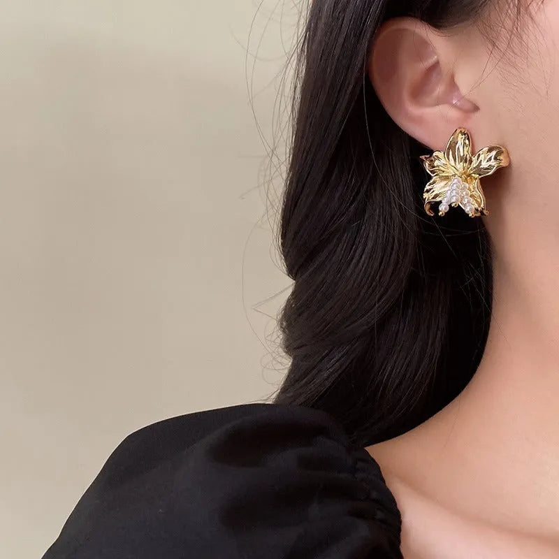 Golden flower-shaped earrings with pearl details on a white background.