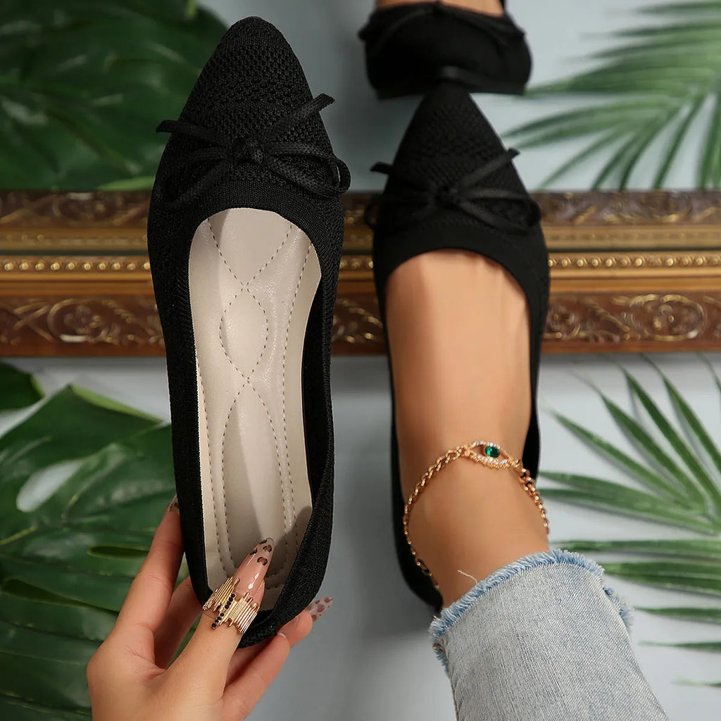 Women's knitted flat shoes with a bow detail and pointed toe in various colours on a plain background.