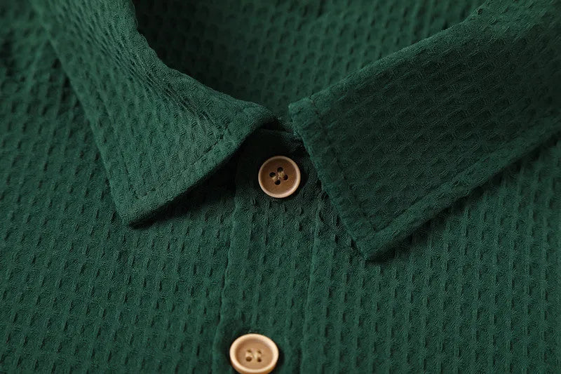 Dark green waffle patterned lapel polo shirt with short sleeves, two round metallic-texture buttons, and slightly arc-shaped hem.