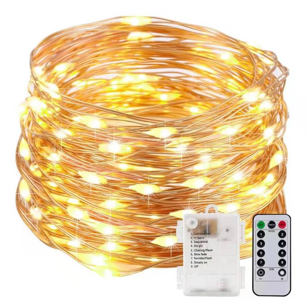 Close-up of bendable copper wire fairy lights with small LEDs, showing battery box and USB cable on a wooden surface.