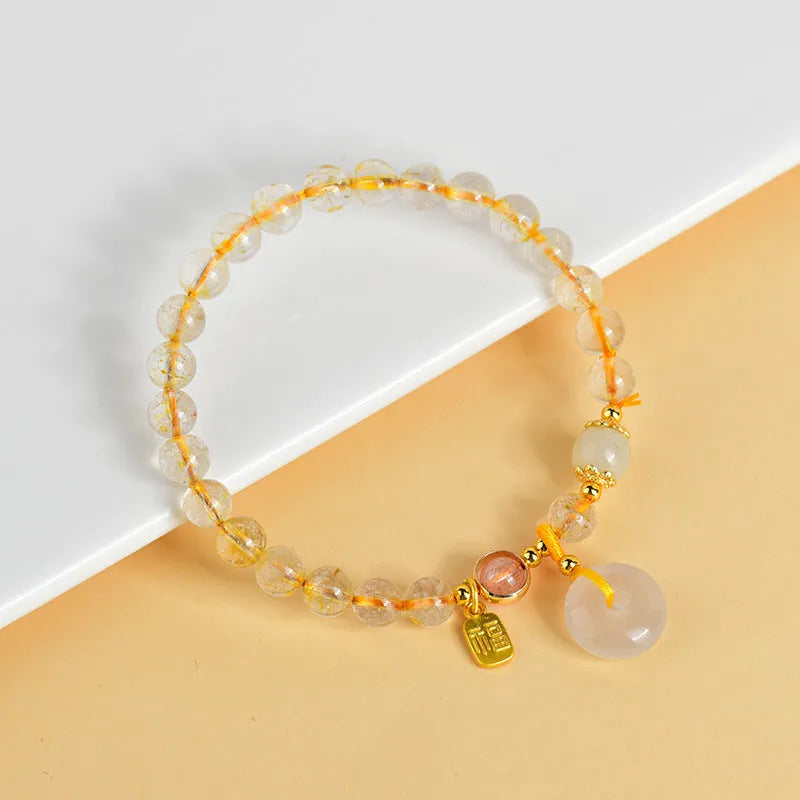 Gold rutilated quartz bracelet with a peace buckle pendant and geometric safety clasp.